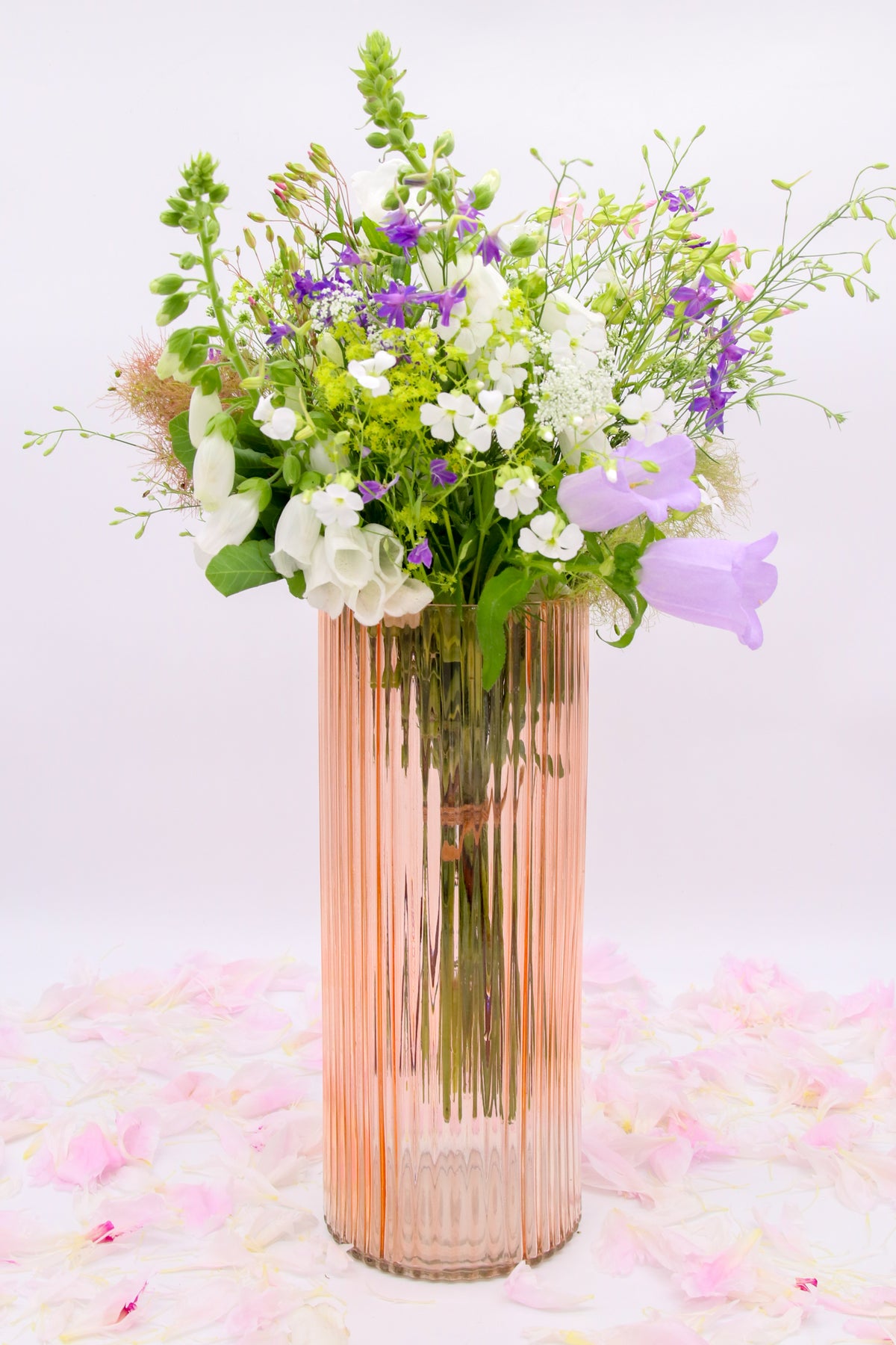 Vase cylindrique rose à fines côtes verticales, présenté avec un bouquet blanc et violet.