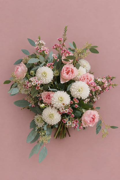 Photo produit du bouquet « Comme au Jardin — Automne » de Rouge Pivoine sur fond rose poudré. La composition champêtre réunit de grandes fleurs blanches rondes, des roses rose pâle et saumon, de petites fleurs roses, des feuillages d’eucalyptus gris-vert et des tiges fines retombantes. Bouquet de saison photographié à plat, avec les tiges visibles au centre bas. Visuel pour commande et livraison de bouquet de fleurs à Caen. Aucun texte ni prix visible.